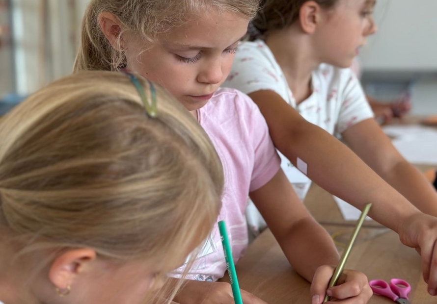 Drei Kinder malen mit Buntstiften Übungszettel aus
